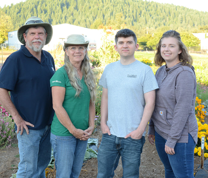 Territorial Seed family leadership standing on their trial farm with flowers, cabbage, and forested hills in the background
