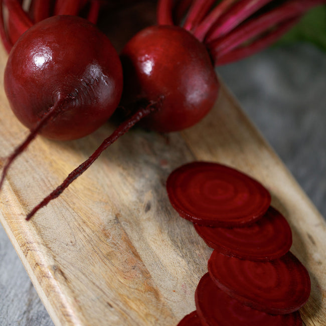 Close-up of Gemini beet showing whole globe-shaped roots and sliced deep-red interior on a wooden cutting board