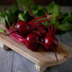 Close up of Gemini beet roots and tops showing dark red smooth globe shaped roots and bright green leaves with magenta veins on a wooden board