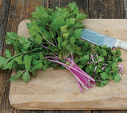Bunch of Chinese Pink celery showing pink and cream streaked stalks and light green leaves on a wooden cutting board