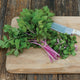 Bunch of Chinese Pink celery showing pink and cream streaked stalks and light green leaves on a wooden cutting board