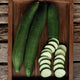Top view of Pepinex English cucumbers, two whole and one partly sliced to show pale flesh and thin dark green skin on a wooden tray
