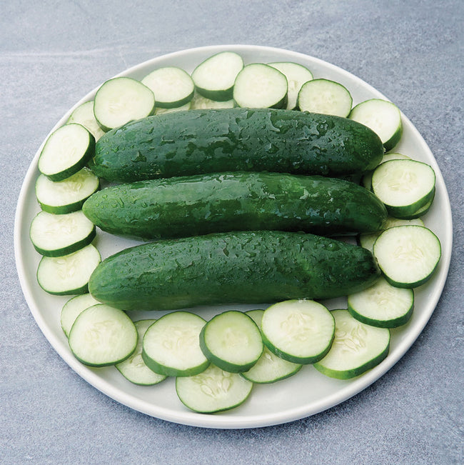Overhead view of Sweet-Slice cucumbers on a plate showing glossy dark green skin and sliced rounds with white interior