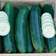 Close-up of three Goliath slicing cucumbers on a wooden board, one sliced to show pale green interior