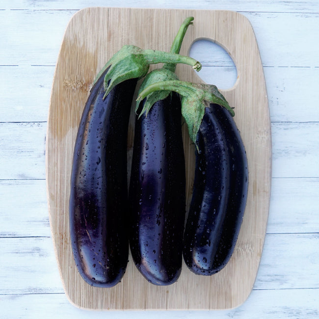 Side view of three Turkish Delight eggplants showing slender glossy dark-purple fruits on a wooden board