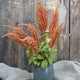 Front view of Hot Biscuits amaranth stems in a blue vase showing apricot plume flower spikes against weathered wood background