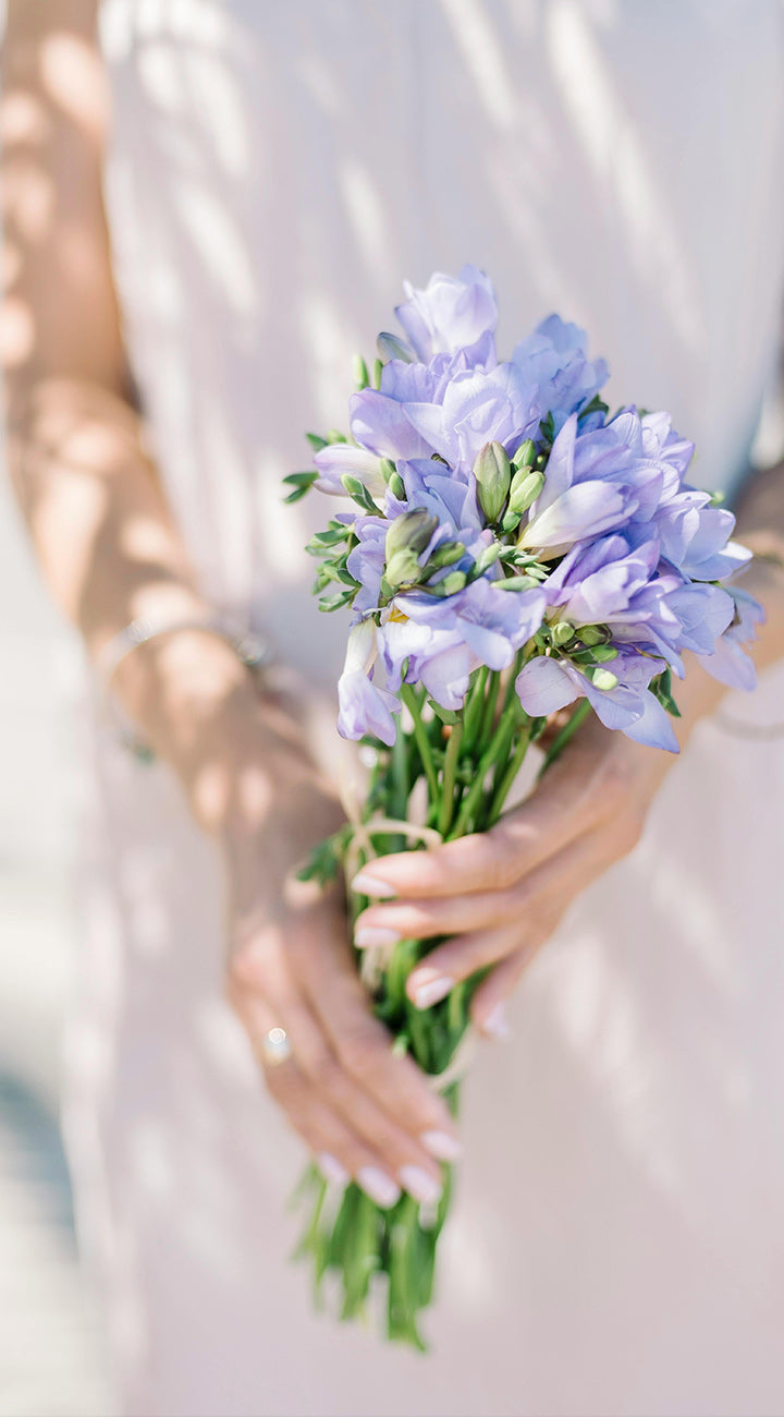 Bouquet of purple Freesia flowers held by a person in a light-colored dress.