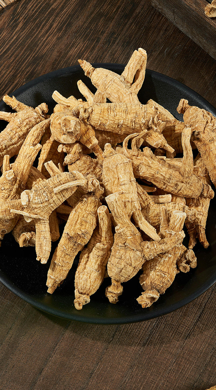 Dried ginseng roots on a black plate with a wooden background