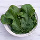 Bowl of green leafy texsel greens kale on a white wooden surface.