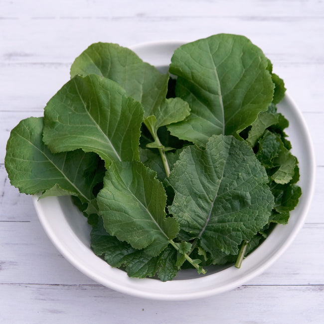Bowl of green leafy texsel greens kale on a white wooden surface.