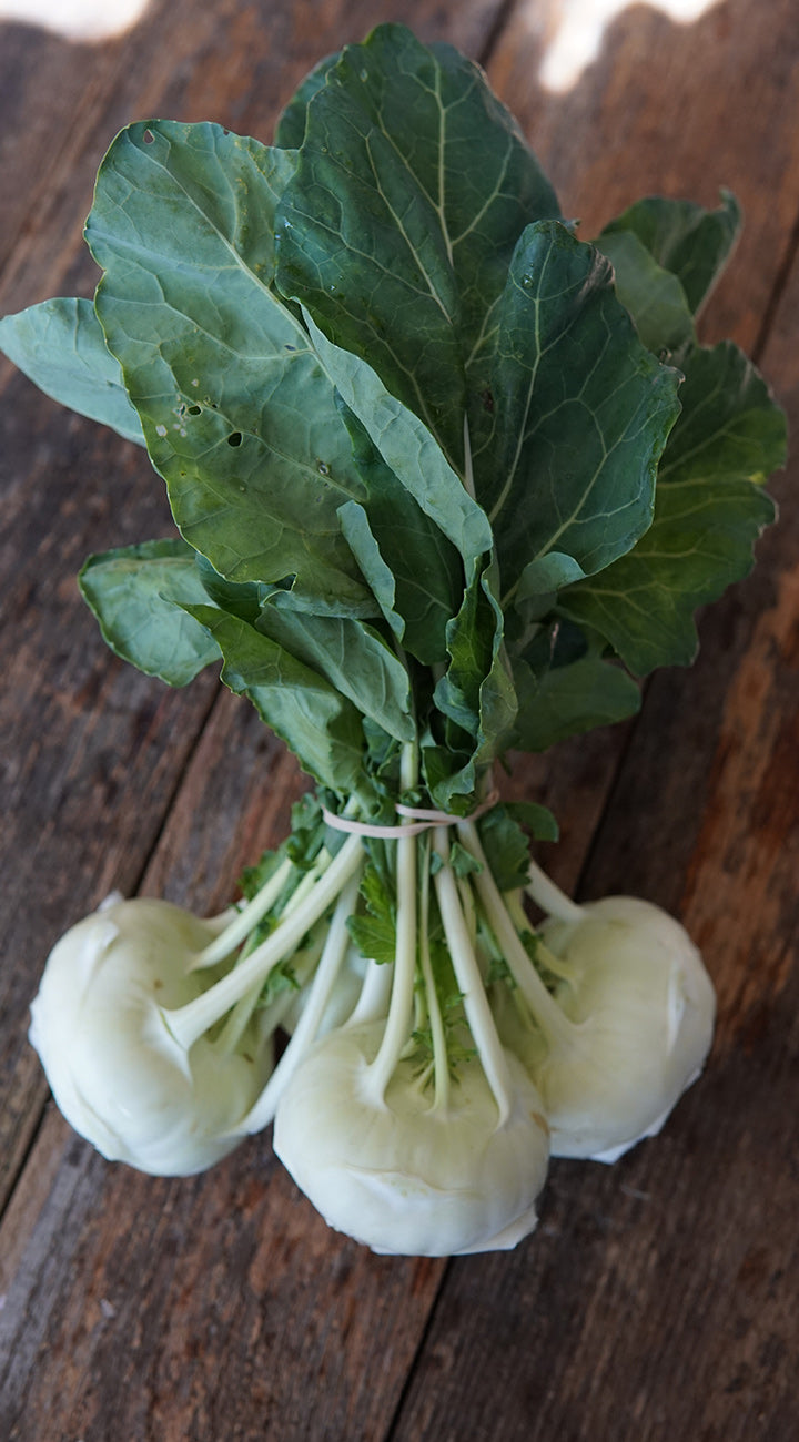 Bunch of white kohlrabi with green leaves on a wooden surface