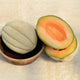 Halved Oregon Delicious cantaloupe showing bright orange flesh and seeds on a wooden bowl