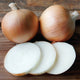 Two whole ovation onions and a few sliced pieces of onion on a wooden surface.