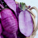 Close-up of purple sweet baby daikon radishes with a wooden basket on a white background