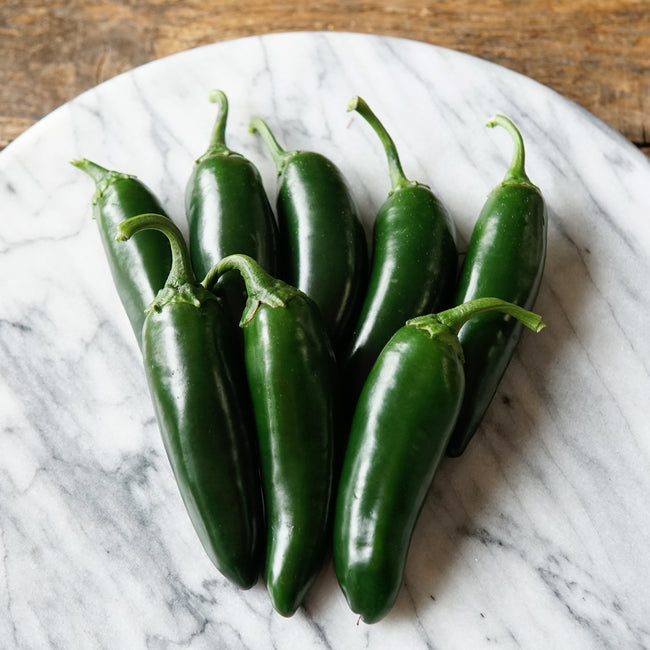 Close-up of Black Magic jalapeño peppers showing deep inky green color and thick walls on a light background