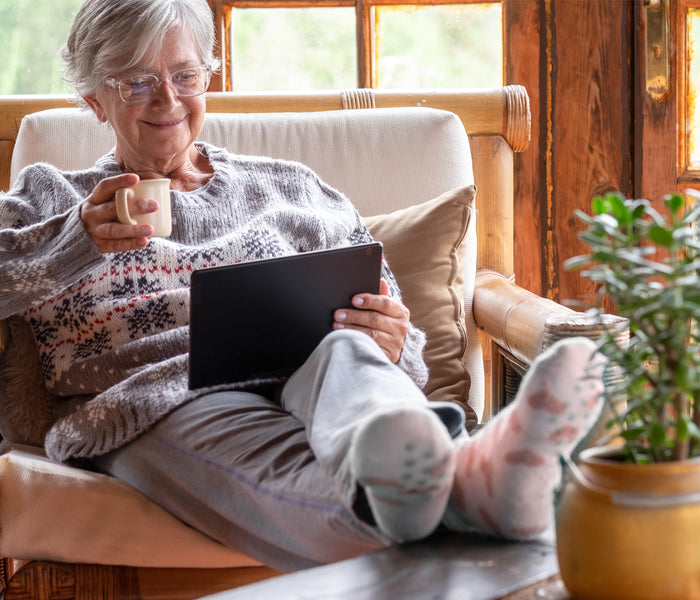 Woman sitting on a couch holding a tablet and a mug, with a plant next to her.