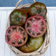 Top-down view of Cappuccino tomatoes showing whole glossy dark chestnut-red fruits with green shoulders and two sliced halves in a wicker basket on a white surface