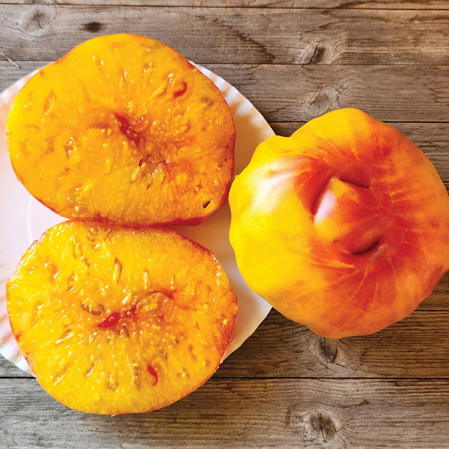 Top-down view of Ginfiz tomato showcasing golden-yellow flesh and red streaks on the skin, arranged on a white plate over a wooden surface