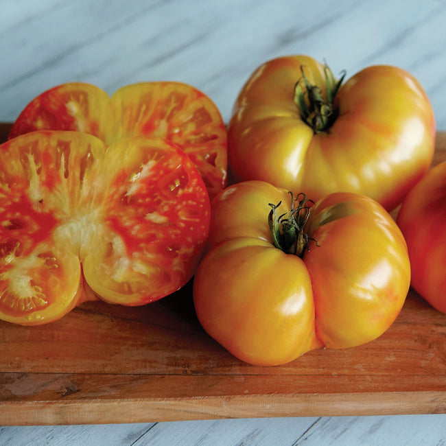 Close-up of Ginfiz tomato fruits showcasing yellow-orange striped skin and sliced interior on a wooden cutting board