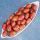 Overhead view of Raspberry Drop grape tomatoes in a white dish, elongated pink-red fruits with water droplets on blue stone