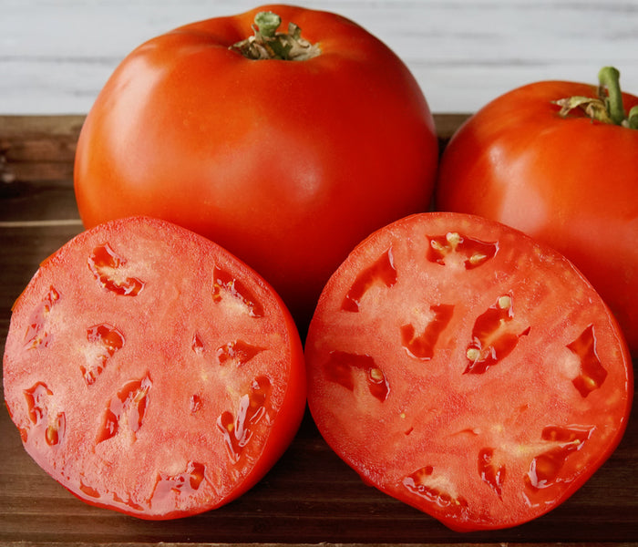 Close-up of Umpqua Beauty heirloom tomatoes, two whole fruits and two cut halves showing meaty red interior on a wooden board