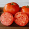 Close-up of Umpqua Beauty heirloom tomatoes, two whole fruits and two cut halves showing meaty red interior on a wooden board