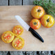 Close-up of Maitai beefsteak tomatoes on a cutting board, one sliced to show golden-yellow flesh blushed with orange