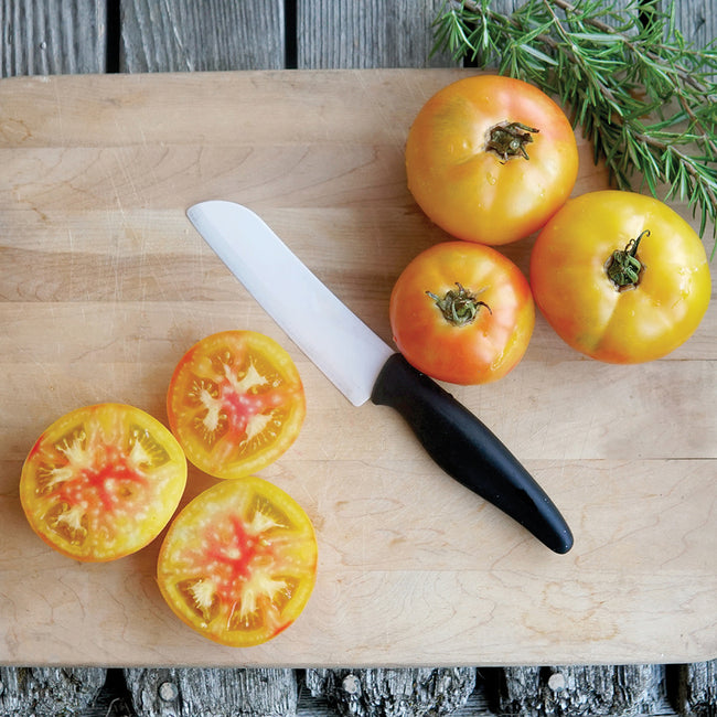 Close-up of Maitai beefsteak tomatoes on a cutting board, one sliced to show golden-yellow flesh blushed with orange