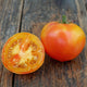 Close-up of Maitai beefsteak tomato showing golden-yellow skin and blushed orange-rose interior on a wooden surface