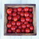 Close-up of Crokini cherry tomatoes in a wooden bowl showing vivid red, glossy, bite-sized fruit on a countertop
