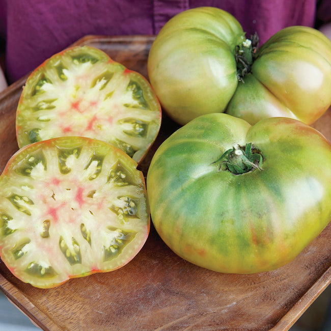 Close-up of Ananas Noire tomato showing multicolored skin and bright green flesh with red streaks on a wooden board