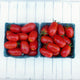 Close-up of Sweet Hearts grape tomatoes in two small baskets showing clusters of oblong red tomatoes on a white wooden background