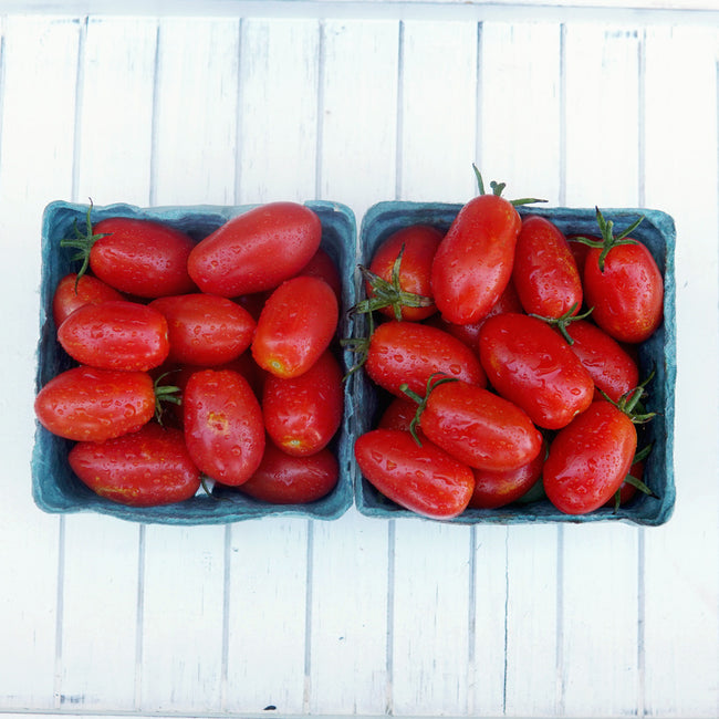 Close-up of Sweet Hearts grape tomatoes in two small baskets showing clusters of oblong red tomatoes on a white wooden background