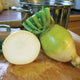 Three-quarter view of Golden Ball turnips with one sliced to show pale, creamy interior on white background