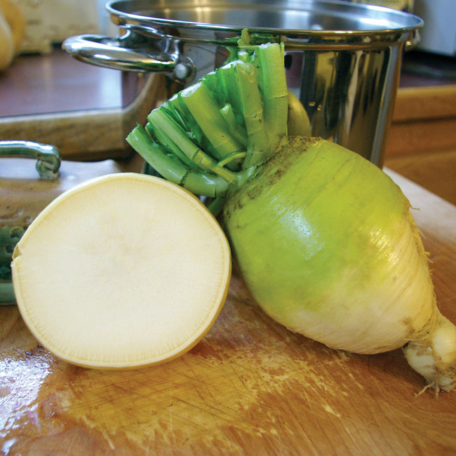 Three-quarter view of Golden Ball turnips with one sliced to show pale, creamy interior on white background