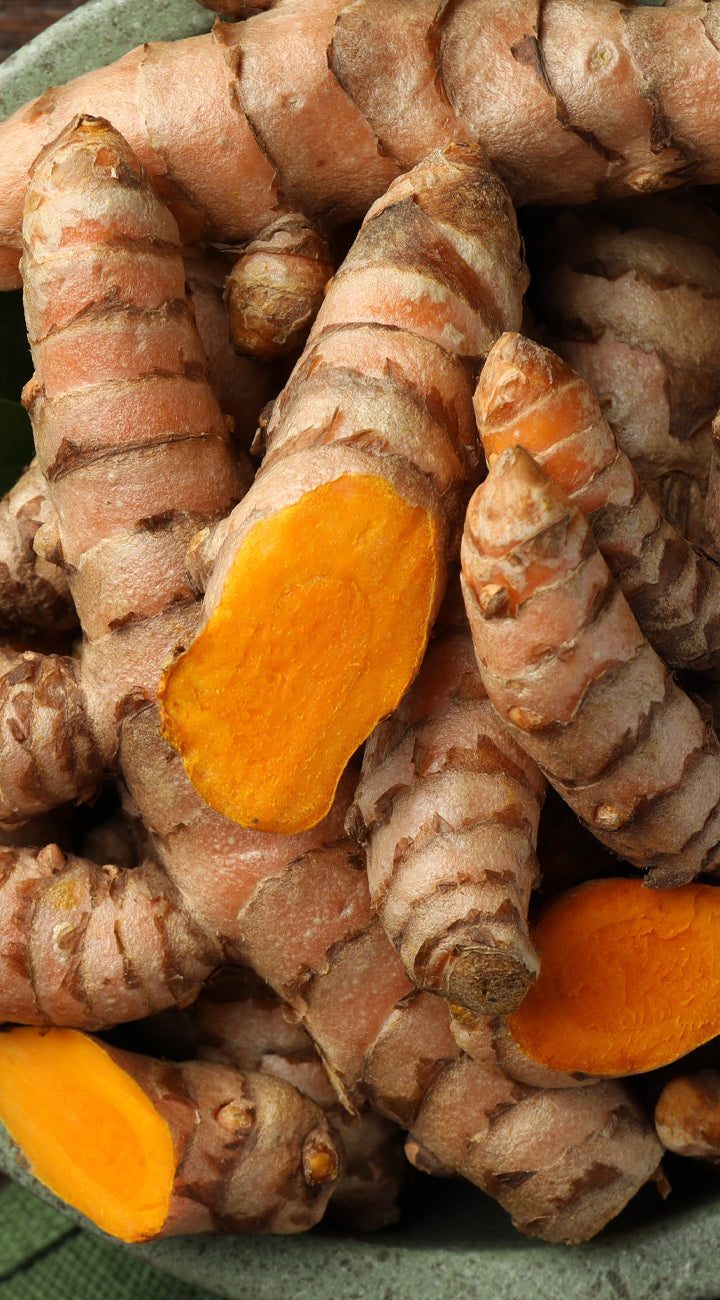 Turmeric roots with bright orange interior on a green surface