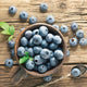 Overhead view of Duke blueberry fruit in a rustic cup showing large light-blue ripe berries on a wooden table