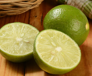 Close-up of Thornless Mexican Key lime showing two cut halves and one whole fruit with glossy thin skin on a wooden surface
