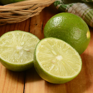 Close-up of Thornless Mexican Key lime showing two cut halves and one whole fruit with glossy thin skin on a wooden surface