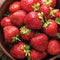 Close-up of Evie-2 strawberry fruit showcasing large glossy red berries with green caps in a wooden bowl