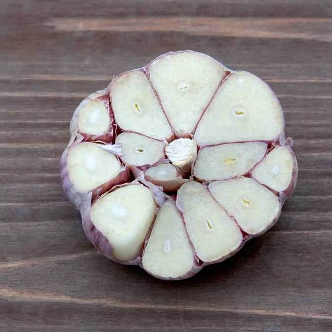 Top view of Persian Star garlic head showing lilac-streaked cloves and white papery wrappers on plain background