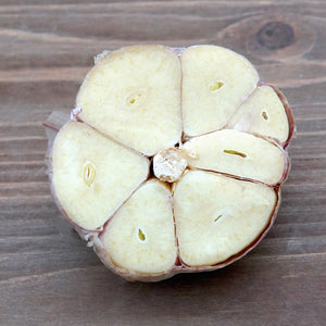 Top-down view of Premium Northern White garlic head cross-section showing large pale cloves on a wooden surface