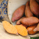 A basket filled with Orleans sweet potatoes, showing smooth, red-skinned tubers with a bright orange flesh inside, freshly cut open to display.