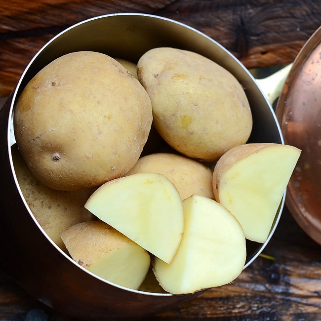 Top-down view of Yukon Gold potatoes, whole and halved, showcasing golden flesh in a copper pan on a wooden surface