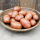 Close up of Désirée potatoes in a bowl showing rosy red skin and smooth, creamy golden flesh on a wooden surface