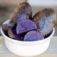 Purple majesty potatoes in a white bowl on a light surface