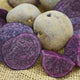 Whole and sliced purple majesty potatoes on a burlap sack surface