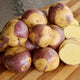 Close-up of Masquerade potato showing purple-mottled skin and yellow flesh with wooden surface background