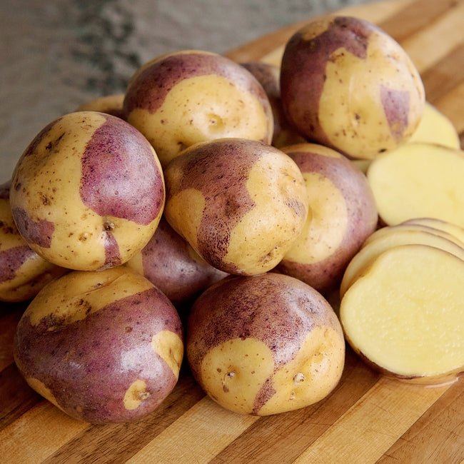 Close-up of Masquerade potato showing purple-mottled skin and yellow flesh with wooden surface background
