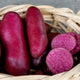 Close-up of Raspberry seed potatoes showcasing red skin and deep red flesh with a sliced tuber on a gray background